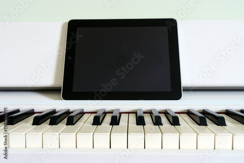 Digital tablet placed on a white piano keyboard, showcasing black and white keys with a minimalistic background and soft lighting enhancing the scene's clarity