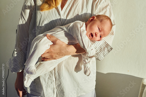 Mother holds newborn baby with soft sunlight in a warm indoor space