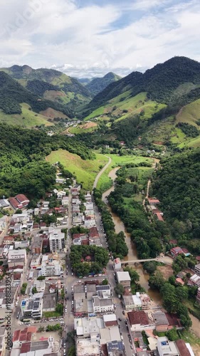 Aerial drone view of Alfredo Chaves city in Espírito Santo, Brazil. Urban area surrounded by green mountains, hills and rural landscape under blue sky, typical countryside scenery.