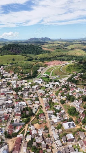 Aerial drone view of Alfredo Chaves city in Espírito Santo, Brazil. Urban area surrounded by green mountains, hills and rural landscape under blue sky, typical countryside scenery.