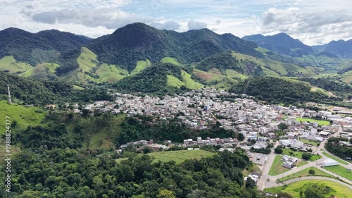 Aerial drone view of Alfredo Chaves city in Espírito Santo, Brazil. Urban area surrounded by green mountains, hills and rural landscape under blue sky, typical countryside scenery.