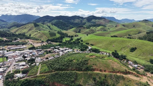 Aerial drone view of Alfredo Chaves city in Espírito Santo, Brazil. Urban area surrounded by green mountains, hills and rural landscape under blue sky, typical countryside scenery.