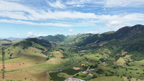 Aerial drone view of Alfredo Chaves city in Espírito Santo, Brazil. Urban area surrounded by green mountains, hills and rural landscape under blue sky, typical countryside scenery.