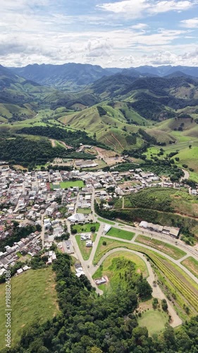 Aerial drone view of Alfredo Chaves city in Espírito Santo, Brazil. Urban area surrounded by green mountains, hills and rural landscape under blue sky, typical countryside scenery.