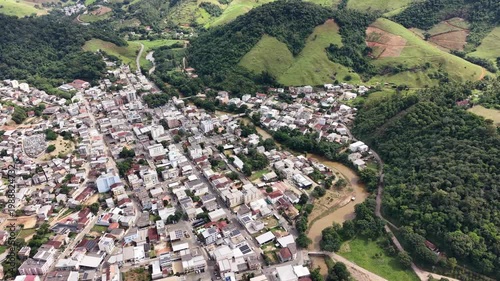 Aerial drone view of Alfredo Chaves city in Espírito Santo, Brazil. Urban area surrounded by green mountains, hills and rural landscape under blue sky, typical countryside scenery.