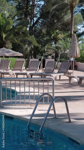 PORTOCOLOM, MALLORCA, SPAIN - OCTOBER, 2025: Empty sun loungers arranged by a swimming pool under midday sun creating sharp contrast and shadows, wide shot