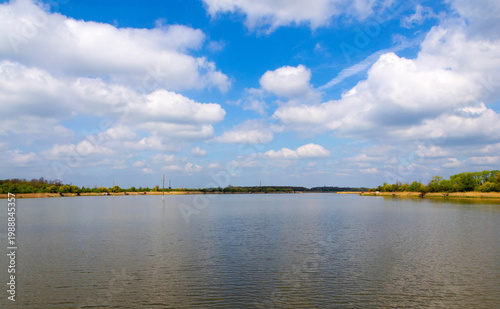 Calm Lake Landscape with Pebble Shore and Blue Sky with Clouds