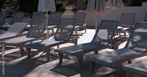 PORTOCOLOM, MALLORCA, SPAIN - OCTOBER, 2025: Bright sun creates strong shadows across empty sun loungers during midday, medium shot
