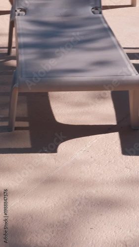 PORTOCOLOM, MALLORCA, SPAIN - OCTOBER, 2025: Midday sun creates strong contrast on empty sun loungers, shadows stretch across the resort patio creating relaxing atmosphere