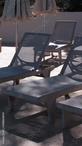 PORTOCOLOM, MALLORCA, SPAIN - OCTOBER, 2025: Bright sun creates strong shadows across empty sun loungers during midday, medium shot
