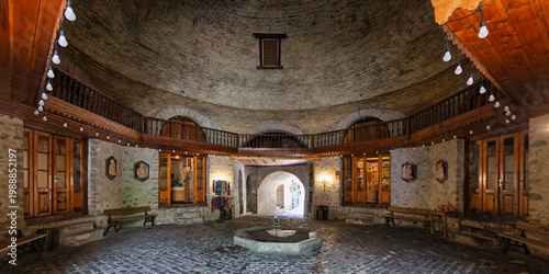 Upper Caravanserai, Shaki, Azerbaijan. Grand circular interior with a domed brick ceiling, wooden balcony, stone walls, cobblestone floor, and central fountain. Historic Silk Road architecture