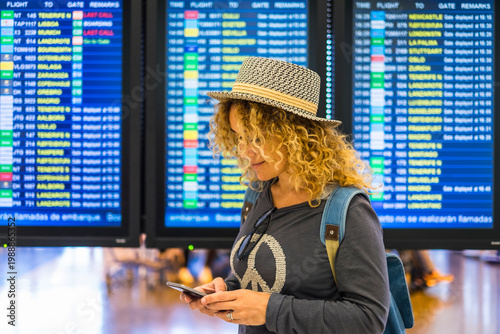 Foto Traveler woman checking phone in airport terminal in front of flight departure b