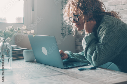 Tableau sur toile Woman working on laptop at home in cozy sweater and glasses, remote work and foc