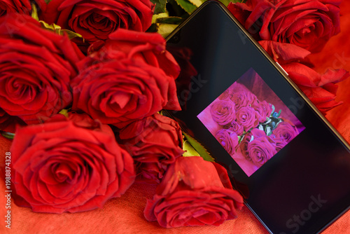 On the smartphone screen is a photograph of a rose lying among real red roses.