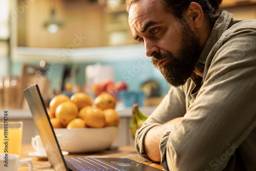 Fotografia Male frowning, laptop screen, disoriented and unsure, uncertain disorganized man, error or misunderstanding at kitchen table