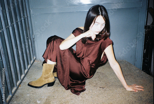 Woman in Brown Dress Sits in Urban Space at Night