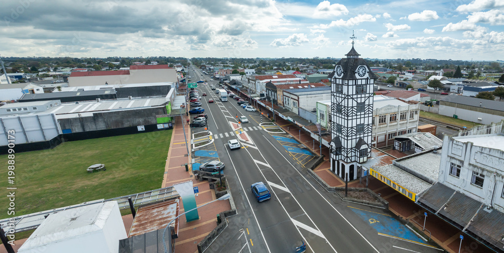 Fototapeta premium A view of the clock tower and street in Statford, Taranaki, New Zealand. Cars drive along the road and park in designated spots.