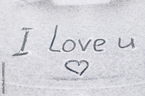 Snow-covered rear window of a car with inscription I love you on it.
