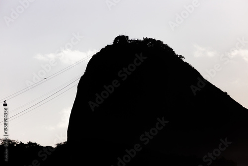 Stunning silhouette of Sugarloaf Mountain in Rio de Janeiro, Brazil, featuring the iconic cable car lines against a bright sky at sunset, a world-famous landmark and tourist destination