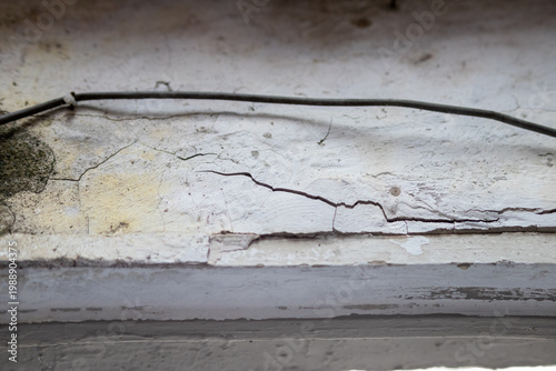 Detailed view of deep cracks and peeling paint on a weathered white concrete surface with a thin black cable, representing structural issues, house maintenance needs, and aged architecture