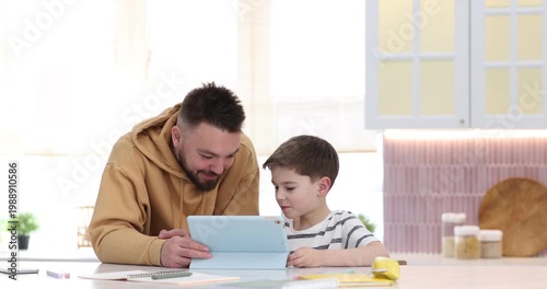 Father and his son using tablet at white table indoors