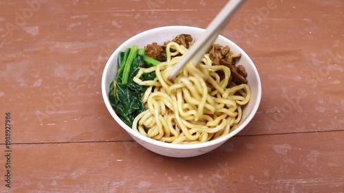 Chicken Noodle (Chicken noodles) is a typical Indonesian noodle dish with minced chicken and boiled mustard greens served on a wooden table with chopsticks. Eat noodles with chopsticks