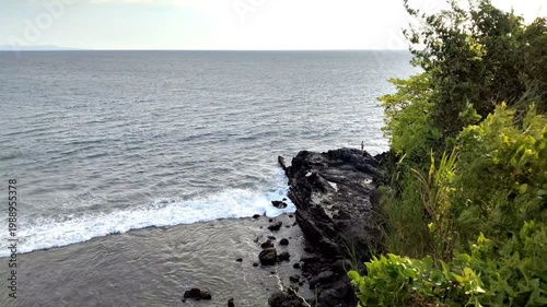A view from above of the large coastal waves crashing against the rocks, which are covered in vegetation