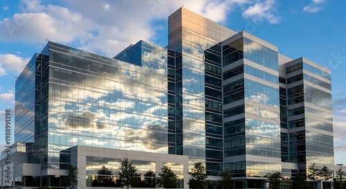 A sleek, modern corporate office building features a striking glass facade, reflecting a dynamic blue sky and white clouds.
