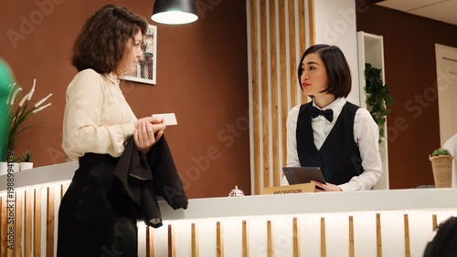 Принти на полотні Hotel guest writing signature on tablet and being handed room card key by asian receptionist during check in process