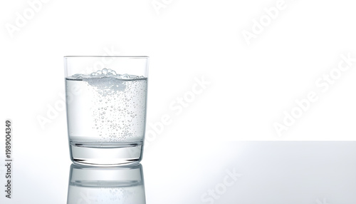 A glass of bubbly water on a reflective surface with a white background