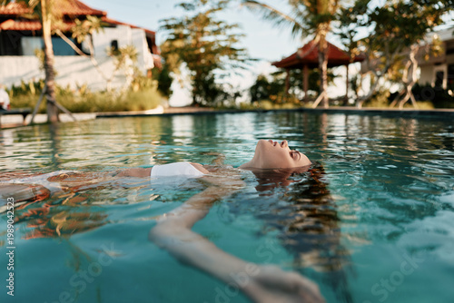Фотография Relaxed woman floats in a calm pool at a tropical resort, enjoying warm sun, gentle water, and a peaceful moment among palm trees