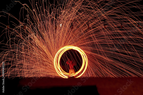 Fotografie The performers are putting on a fire-spinning show on the beach at night, creating beautiful streaks of light and bright orange sparks swirling in circles against the nighttime backdrop