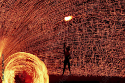 Fotografie The performers are putting on a fire-spinning show on the beach at night, creating beautiful streaks of light and bright orange sparks swirling in circles against the nighttime backdrop