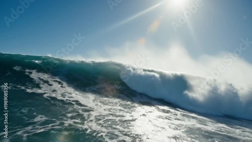 A massive wave crashes powerfully in the ocean on a sunny day with clear blue skies and spray forming.