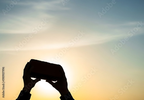 Silhouette of hands holding a brick against the sunset sky