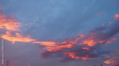 Sky shows bright colors during sunset as the sun goes down. Clouds reflect orange and pink hues as it gets darker. Lights begin to fade away in the distance.