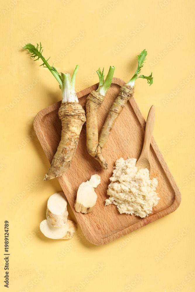 Fototapeta premium Wooden board with horseradish sauce, roots, slices and spoon on yellow background