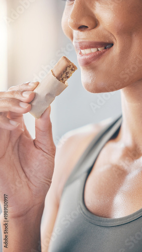 Woman eating healthy snack bar during fitness routine indoors smiling