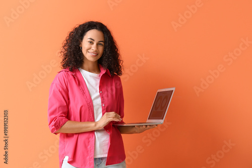 Female African-American interior designer with laptop on orange background