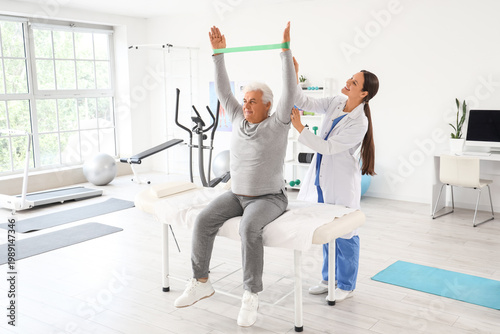Senior man training with stretching band and therapist in rehabilitation center