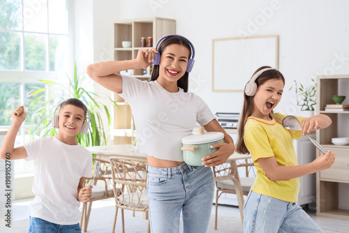 Young mother and her children in headphones with kitchen utensils at home