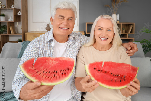 Mature couple with slices of watermelon sitting on sofa at home