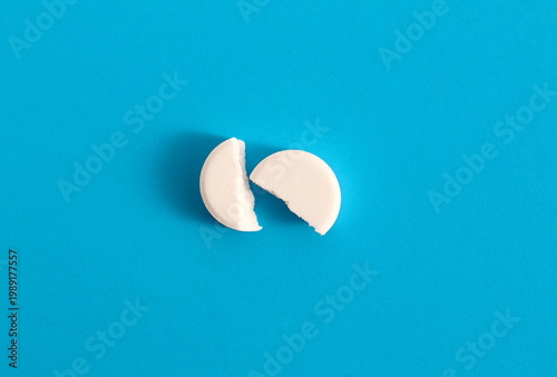 Bild auf Leinwand On a blue background lies a white medicine tablet broken in half.