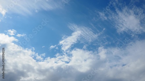 Clouds move across a blue sky over a city in the afternoon. The light changes as some clouds block the sun. Patterns form as the sky shifts.