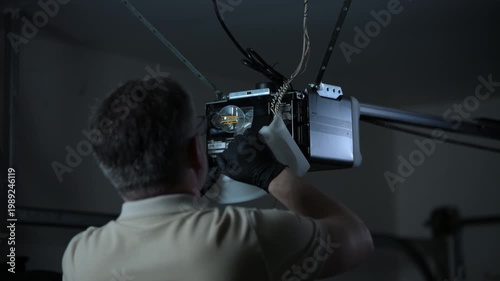 ServiceMan repairing garage door opener. Technician connecting wires on ceiling mounted motor in residential garage.