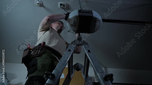 ServiceMan repairing garage door opener. Technician checks wires on ceiling mounted motor in residential garage.