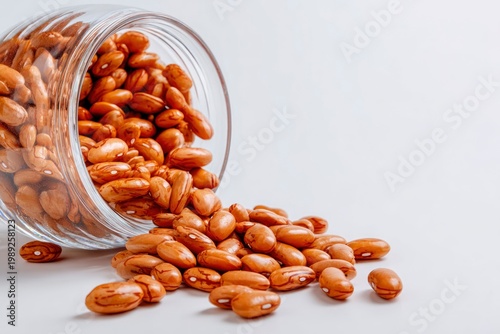 Raw pinto beans spilling out of a glass jar, dry mottled brown beans isolated on a white background.