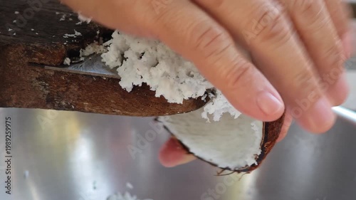 Traditional way, housewife sit on wooden coconut grater and grate coconut into container