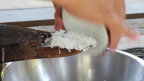 Traditional way, housewife sit on wooden coconut grater and grate coconut into container