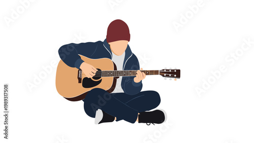 Young man wearing a beanie and jacket sitting on the floor and playing a wooden acoustic guitar with passion.